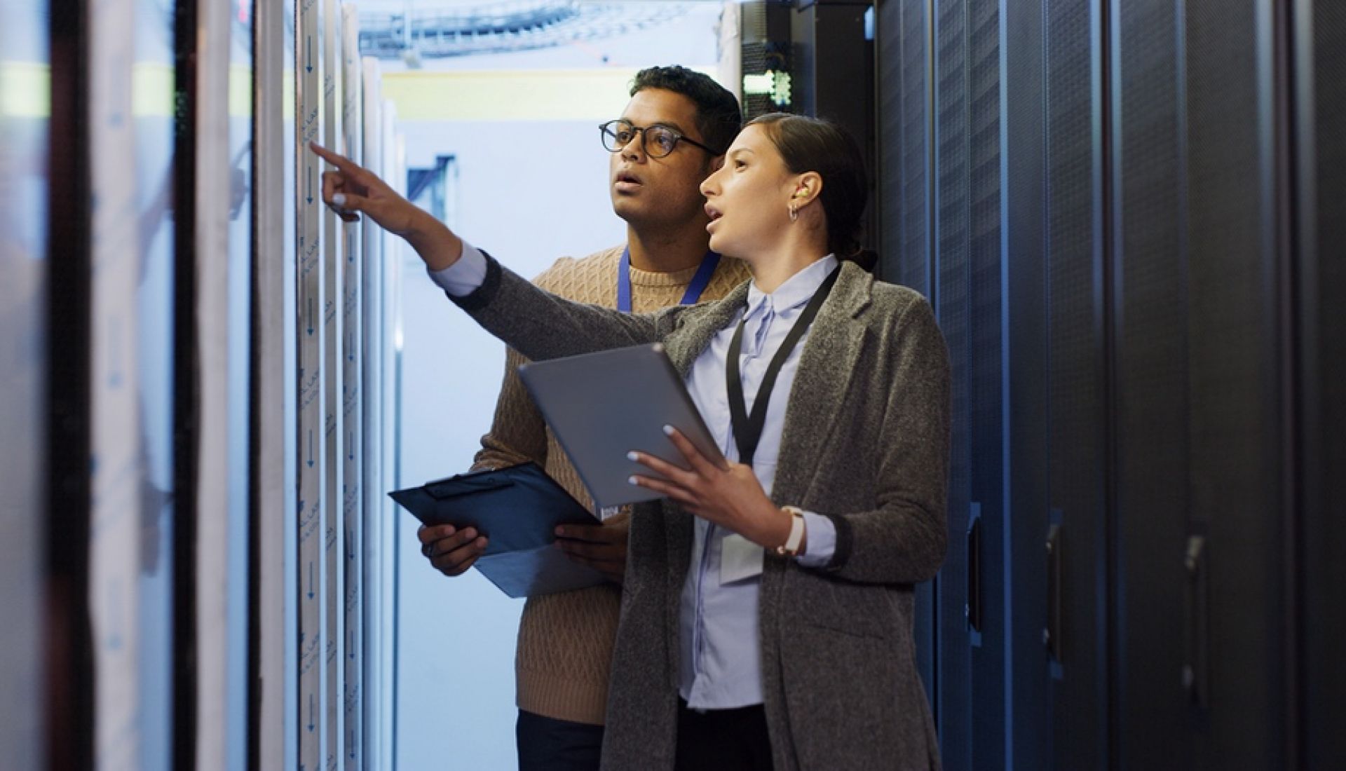 Medium shot of technicians working on a laptop in a data center full of rack servers running diagnostics and maintenance on the system